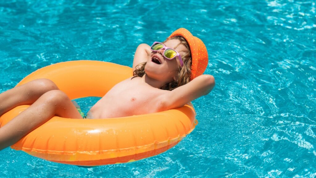 Child in swimming pool on inflatable float ring. Water toy, healthy outdoor sport activity for children. Kids beach fun.