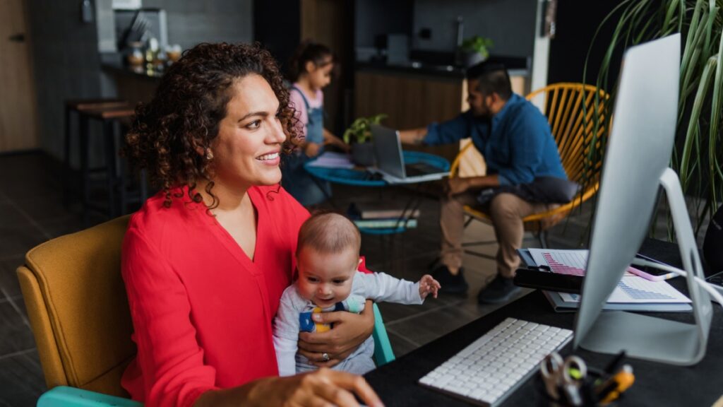Hispanic mother using computer to work at home while she takes care of his baby son in Mexico Latin America, home office concept.