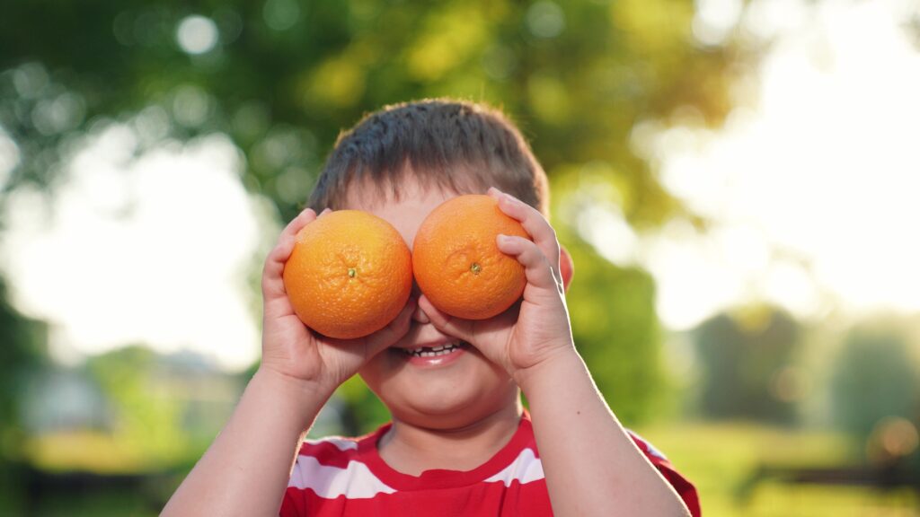 Fruit vitamins for kid boy from garden. Healthy food. Boy kid plays with fresh juicy oranges. Cute child is holding orange slices like orange glasses. Concept of healthy eating for child. Happy family.